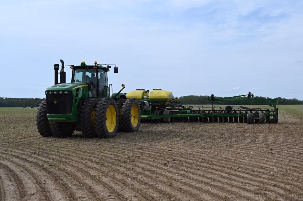 A large combine harvester working in a vast field of ripe soybeans under a clear sky.