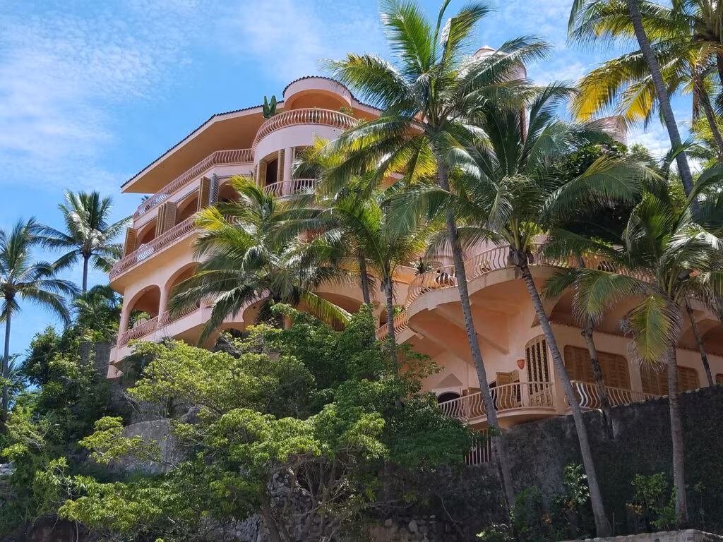 A large, luxurious mansion in the Bel-Air neighborhood of Los Angeles, surrounded by palm trees and sunshine.