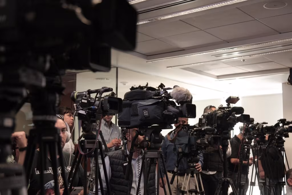 A news reporter standing in front of a camera in a television studio, symbolizing the staff affected by the CBS News layoffs.