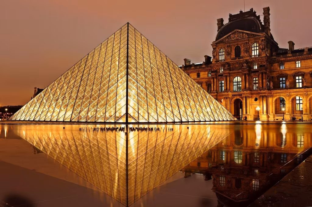 Exterior view of the Louvre Museum in Paris with the glass pyramid and security personnel nearby.