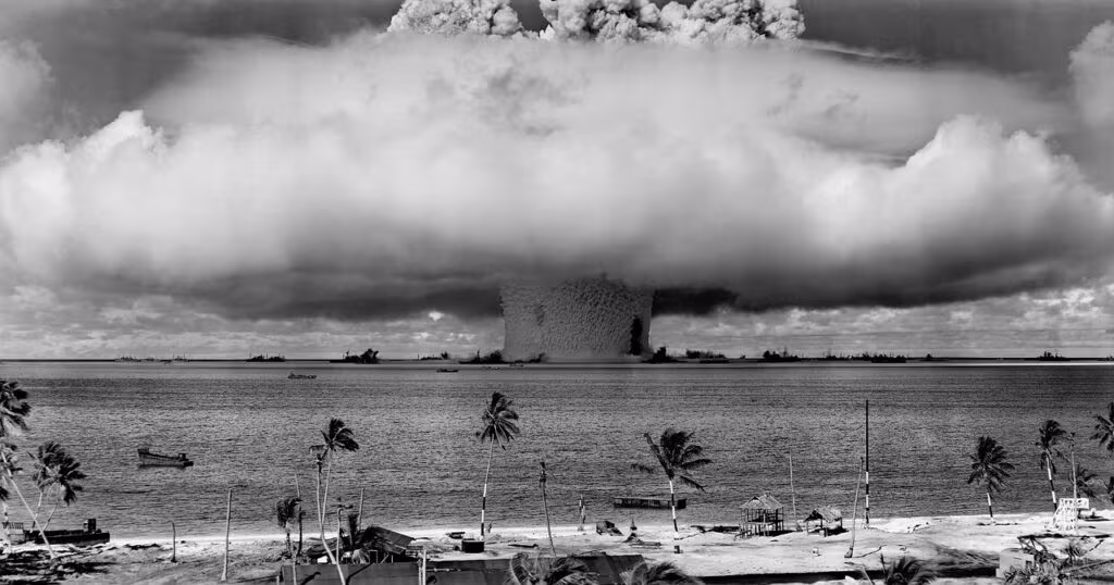 Historical image of a nuclear test mushroom cloud over a desert landscape.