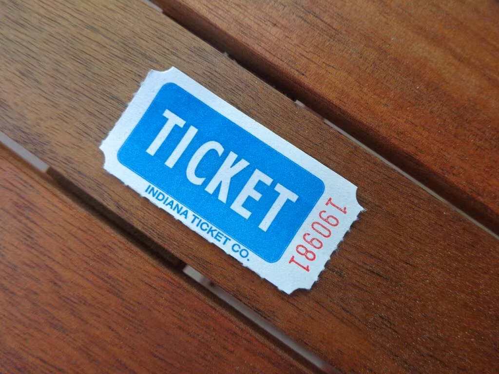 A hand holding a pencil filling out a Mega Millions lottery ticket with selected numbers.