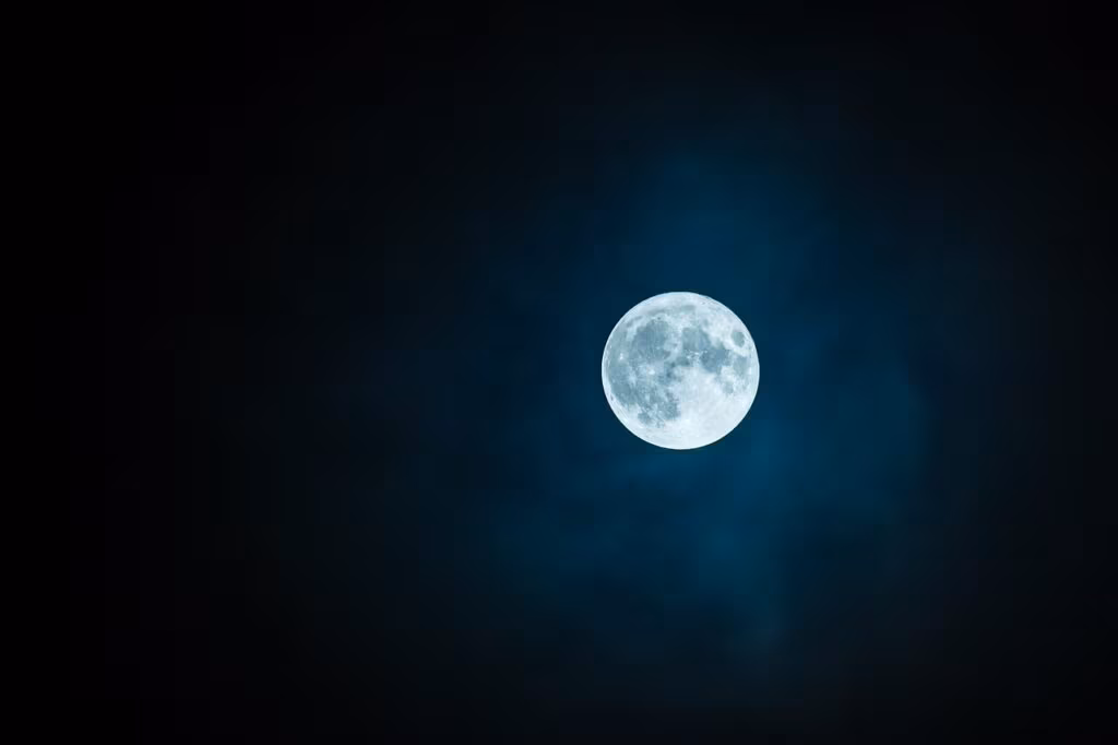 A person looking through a telescope at the bright full moon in a clear night sky.