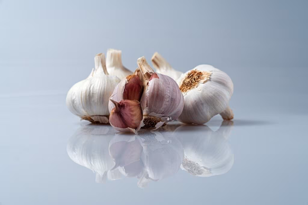 A pile of fresh garlic cloves and bulbs on a wooden cutting board in a kitchen setting.