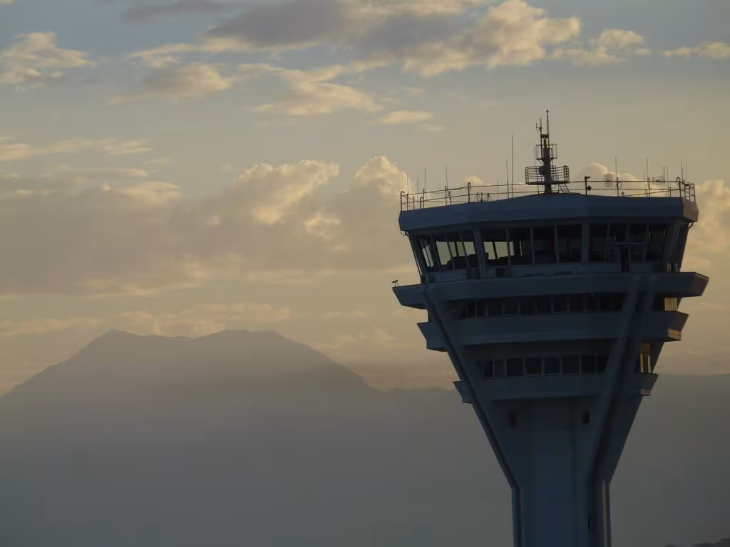 Air traffic control tower silhouetted against the sunset at a busy airport, symbolizing operational stress.