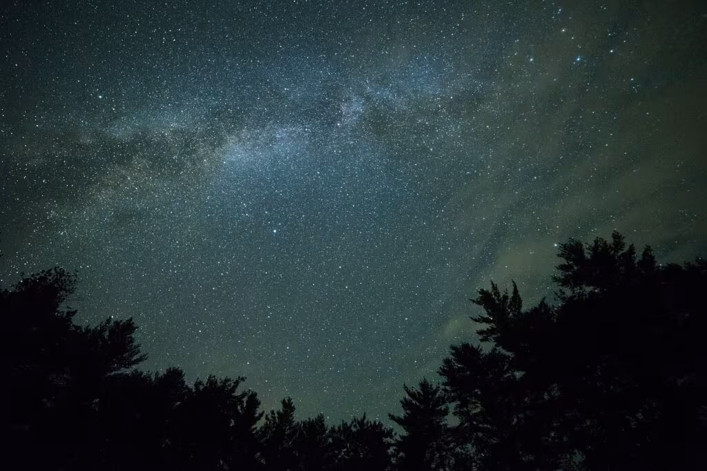 An observer sitting in a dark field using a reclining chair to watch the night sky for meteors.