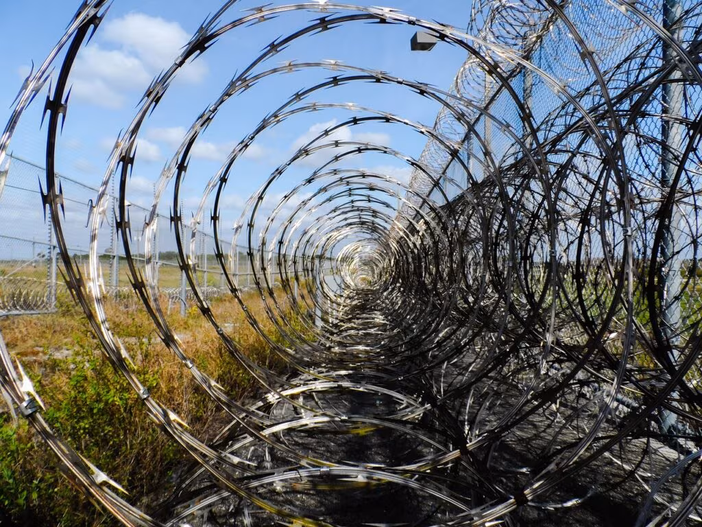 Exterior view of a high-security federal correctional facility with fences and guard towers.