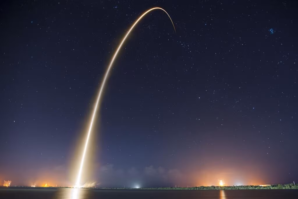 Falcon 9 rocket lifting off from Cape Canaveral at night, illuminated by engine fire.