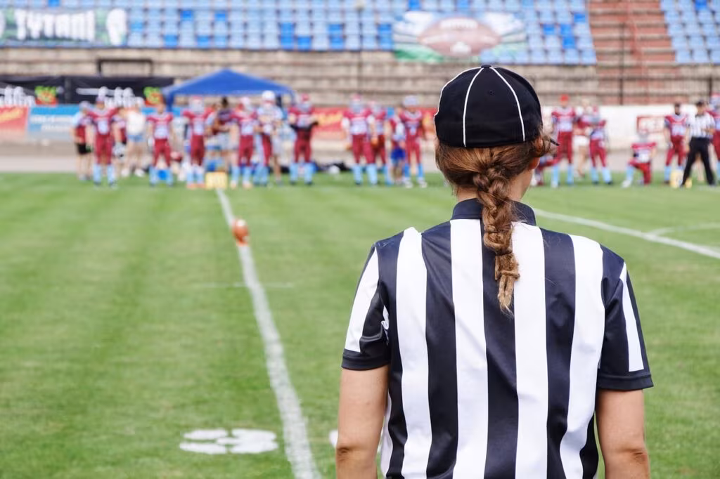 NFL coach wearing a headset on the sideline during a game, focusing intently on the field.