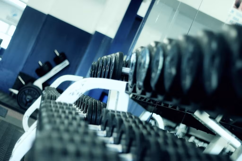 Older adult performing resistance training with dumbbells in a gym setting.