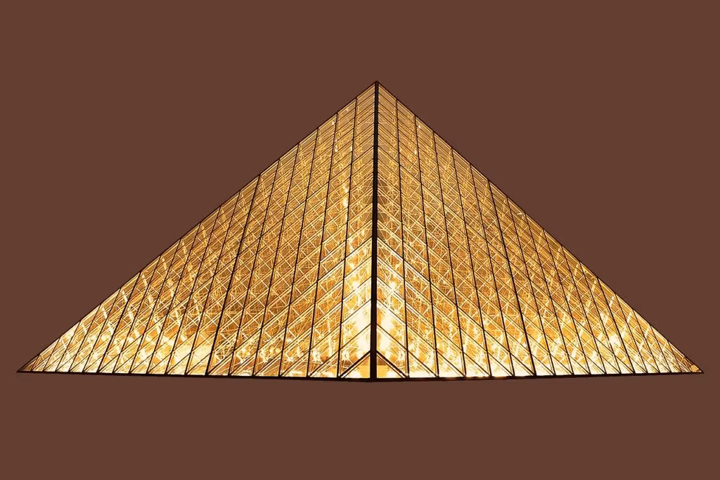 The iconic glass pyramid entrance of the Louvre Museum in Paris, France, bustling with tourists.